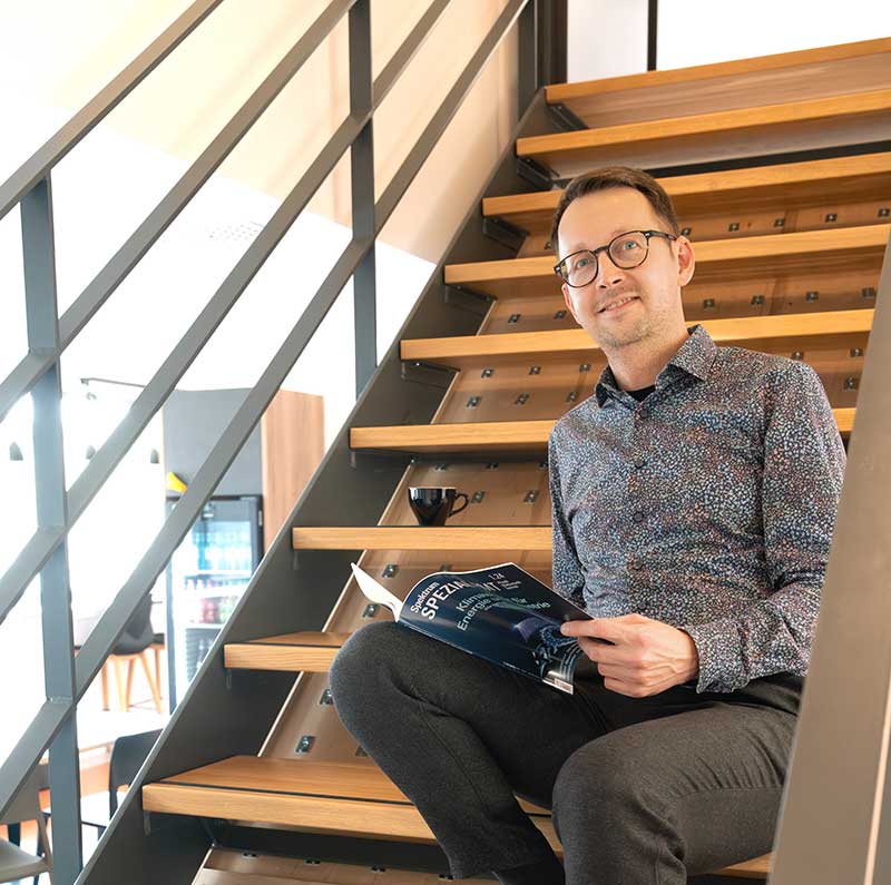 Person sitzt auf einer modernen Holztreppe in einem Innenraum und liest ein Magazin.